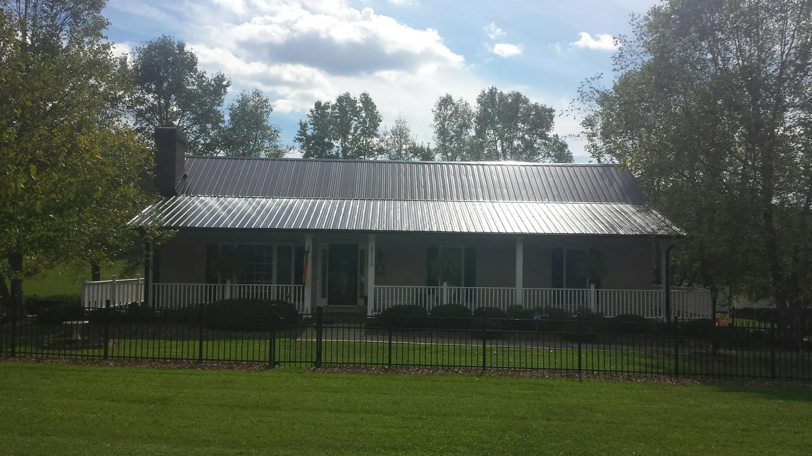 Gray metal roof on a brick ranch with a full width front porch — Gutter Guard Installation work by our crew in Utica